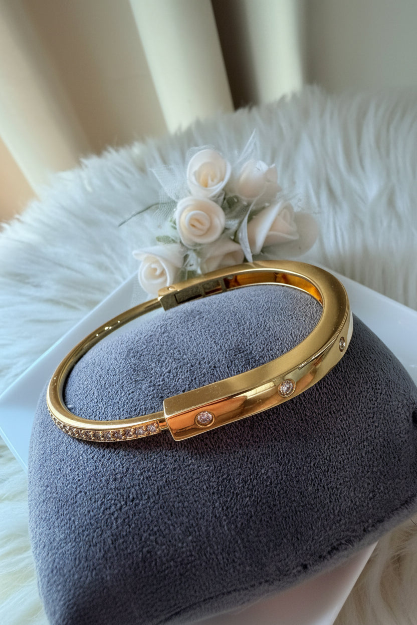 A gold-toned metal cuff bracelet with a sliding clasp and small clear stones, 