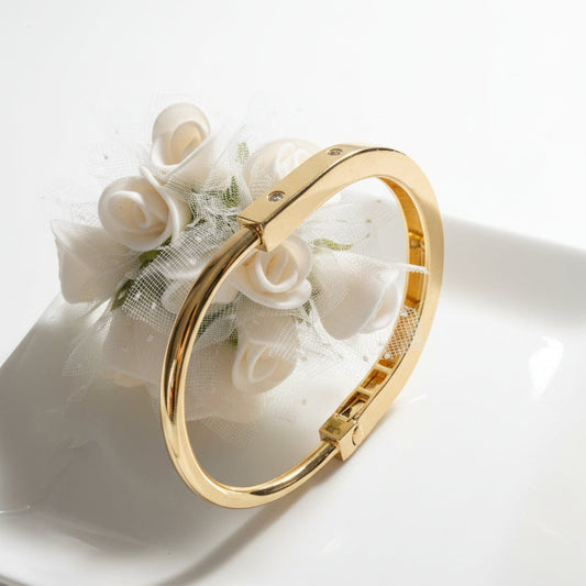 A polished gold-toned metal bangle bracelet with a square hinge clasp