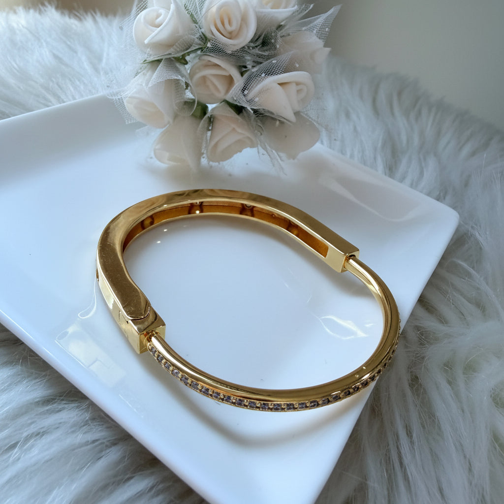 A gold-toned bangle bracelet with a small row of clear stones